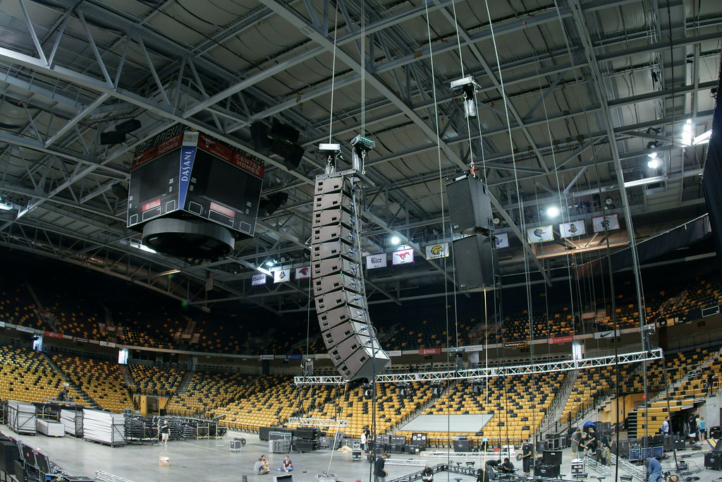 A hanging line array of loudspeakers suspended above an arena floor.